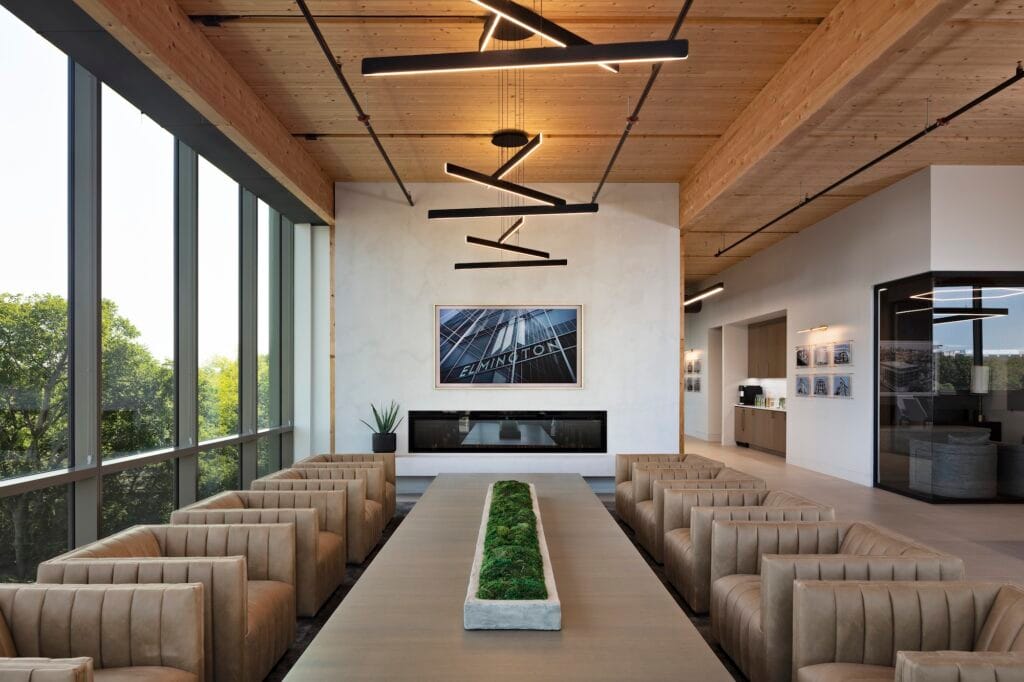 Linear lights set in a triangle hang from aircraft cable cord over a casual office conference area